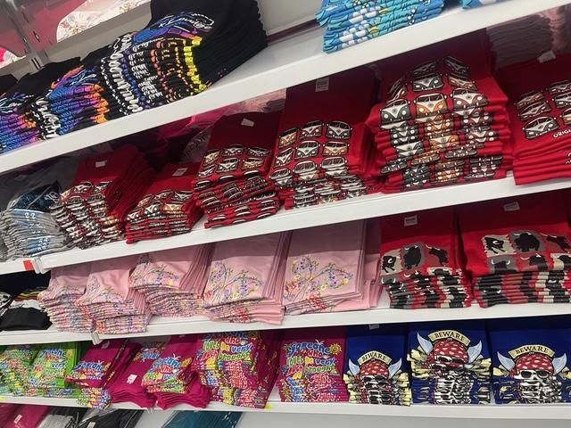 Estantes de camisetas dobladas en varios colores y diseños en una tienda.