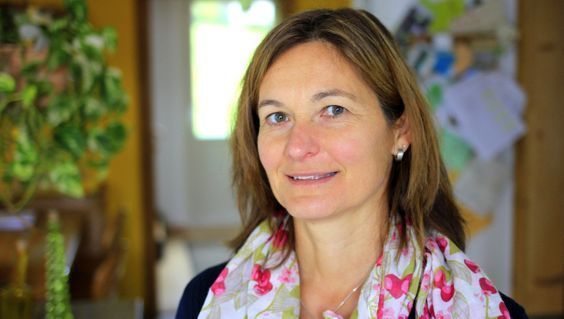 Eine Frau mit Schal und Ohrringen lächelt in die Kamera.