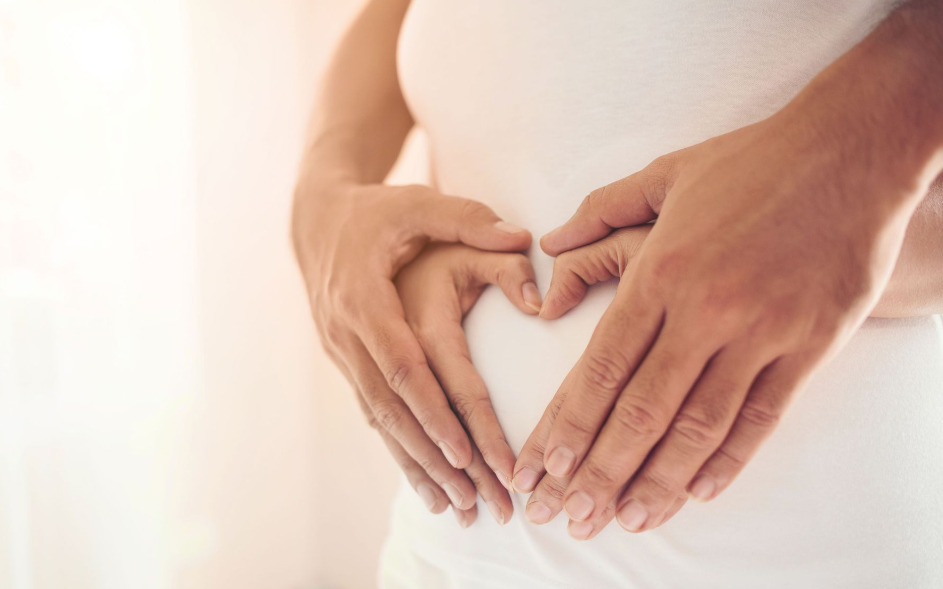 Eine schwangere Frau formt mit ihren Händen auf ihrem Bauch ein Herz.
