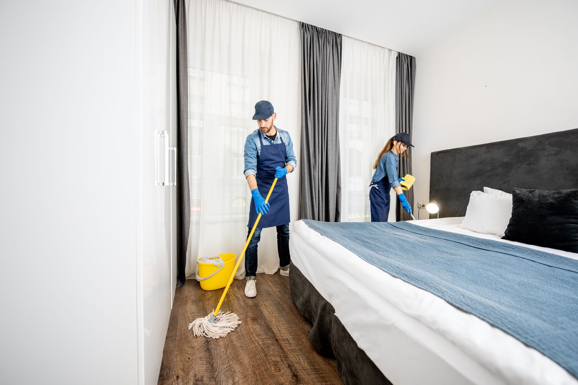 Agents de nettoyage professionnels en uniforme nettoyant les sols et dépoussiérant les meubles d'une chambre d'hôtel