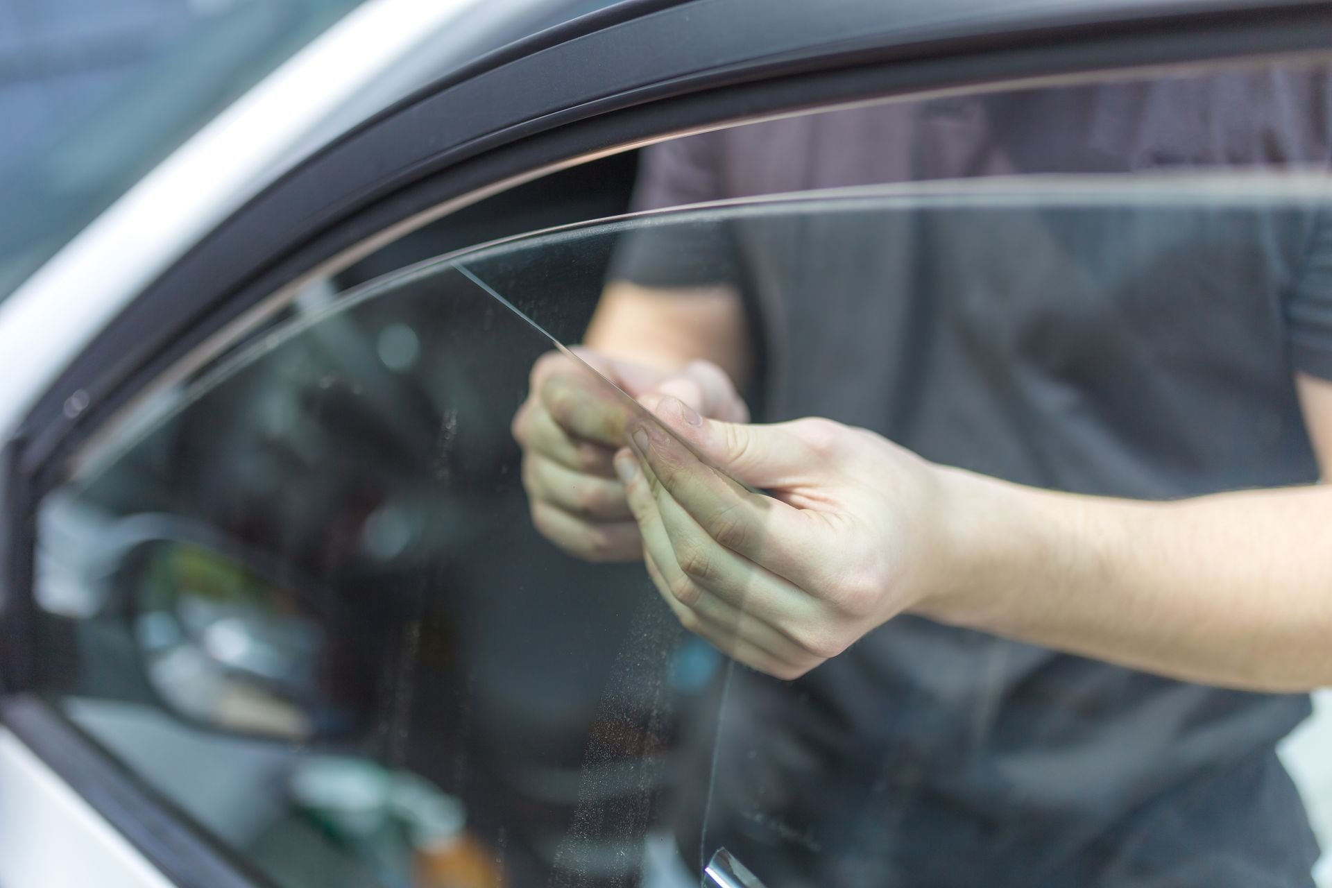 Des mains polissent la vitre d'une voiture avec un chiffon, vues à travers le verre.