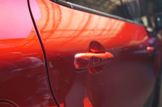Gros plan sur une portière de voiture rouge et sa poignée avec des reflets lumineux.