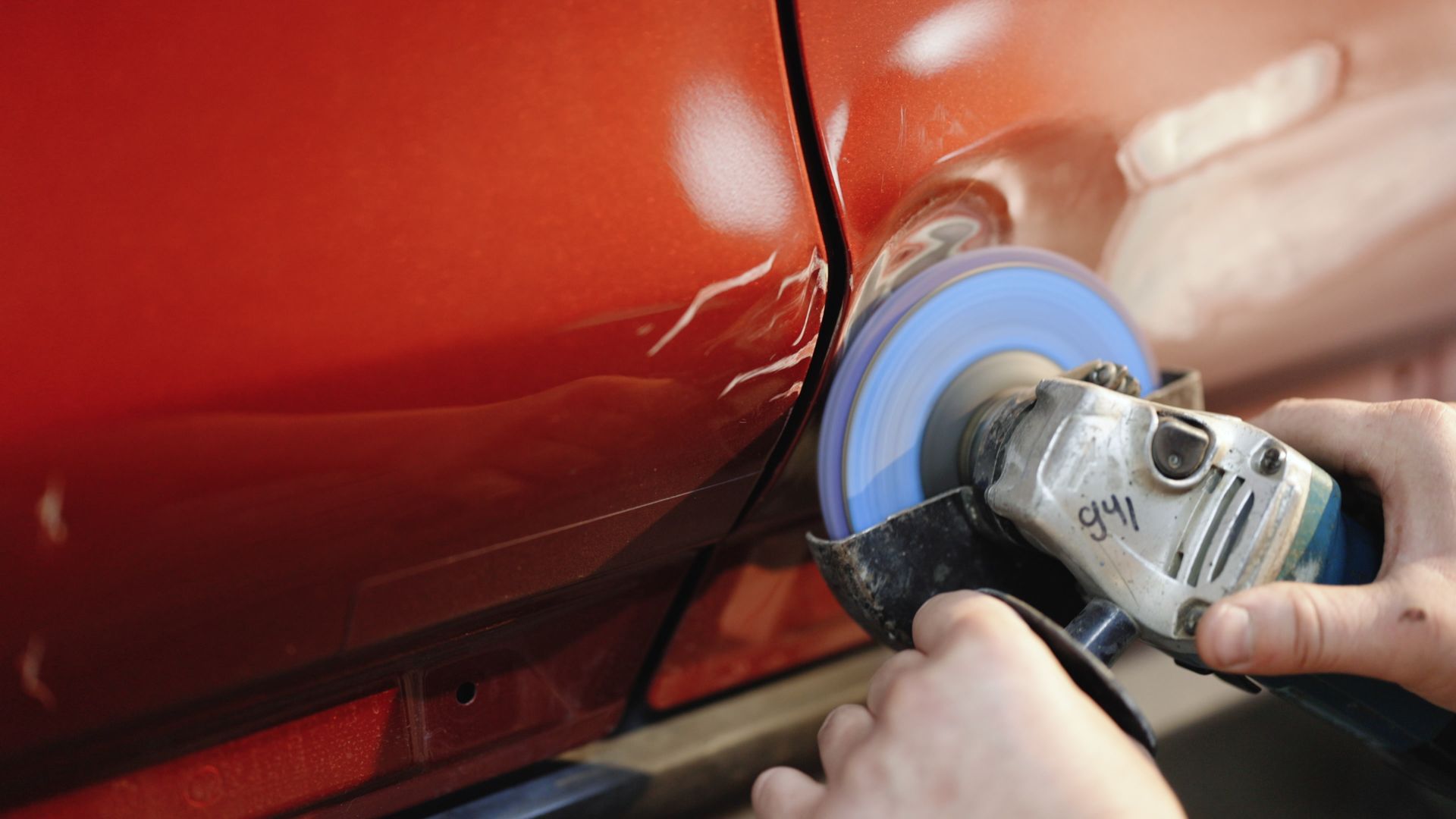 Main utilisant une ponceuse rotative pour polir un panneau de porte de voiture rouge