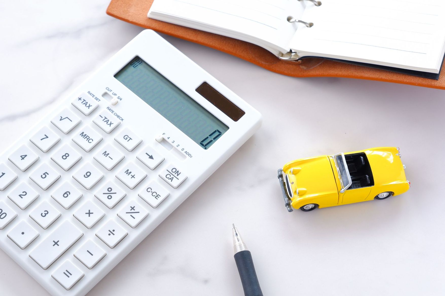 Une calculatrice, une petite voiture jaune et un stylo sur un bureau avec un cahier ouvert.