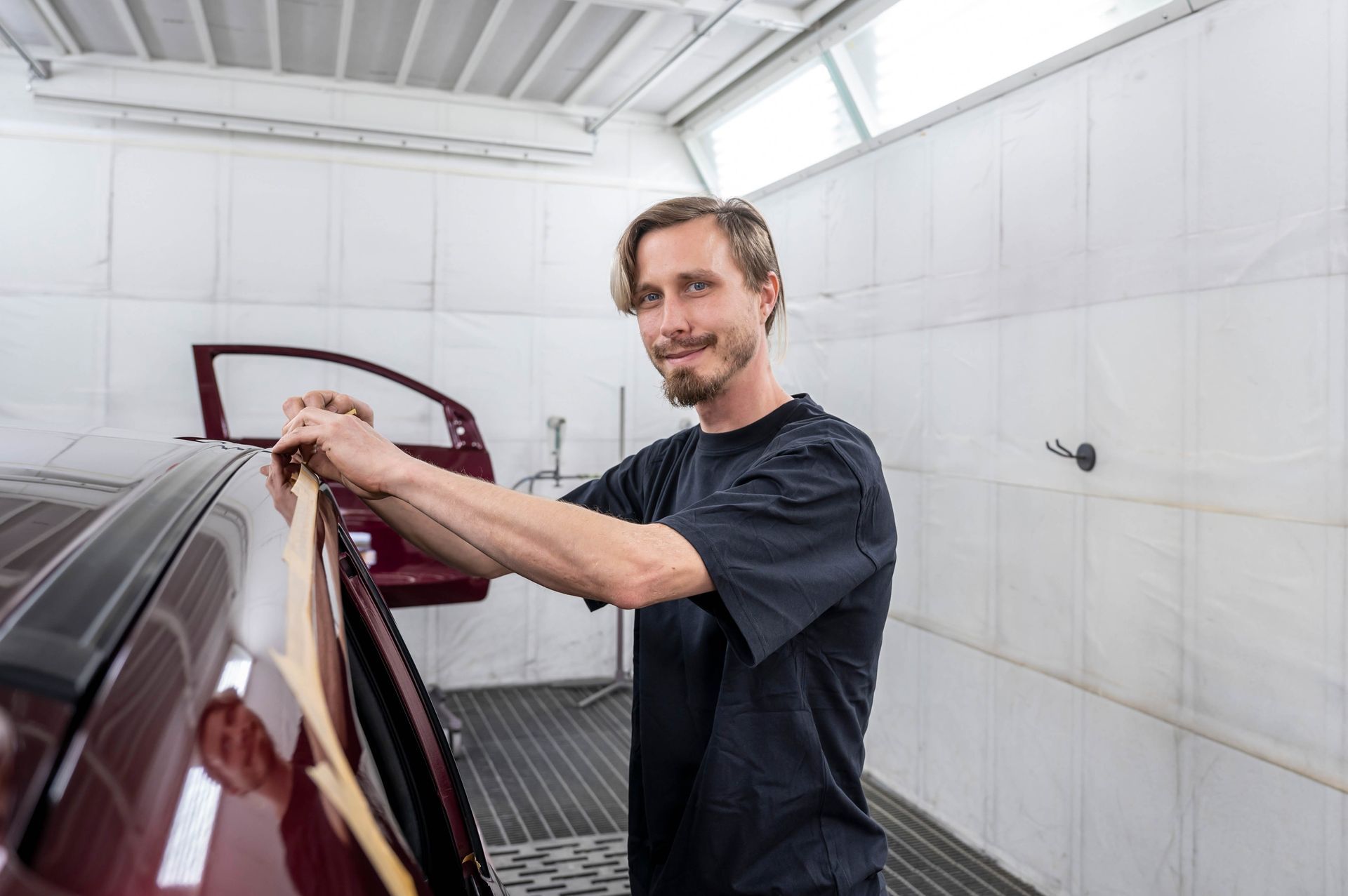 Mann filmt Auto in Autowerkstatt; er lächelt in die Kamera.