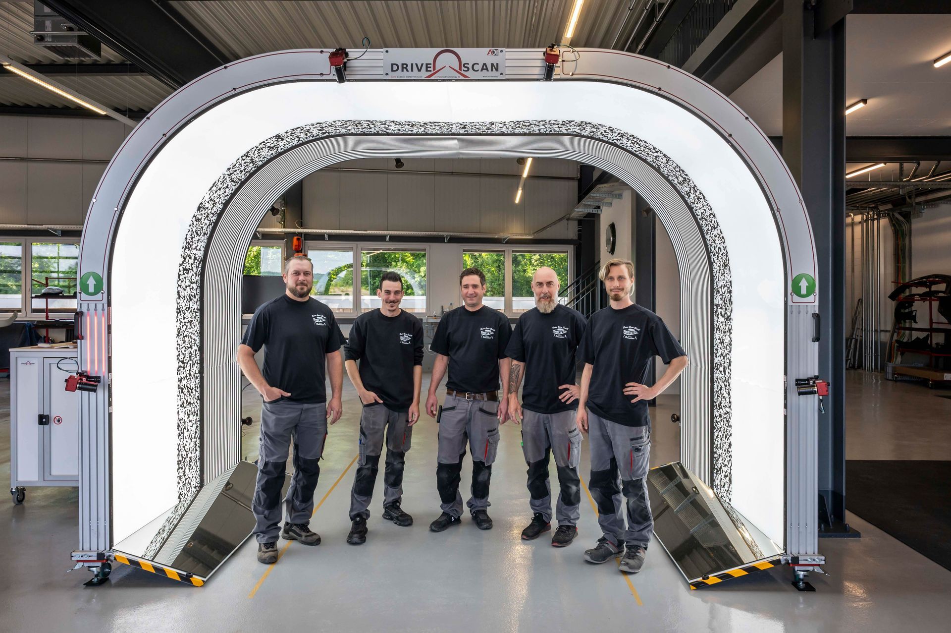 Fünf Männer in Arbeitskleidung posieren in einer Werkstatt vor einer bogenförmigen Maschine.