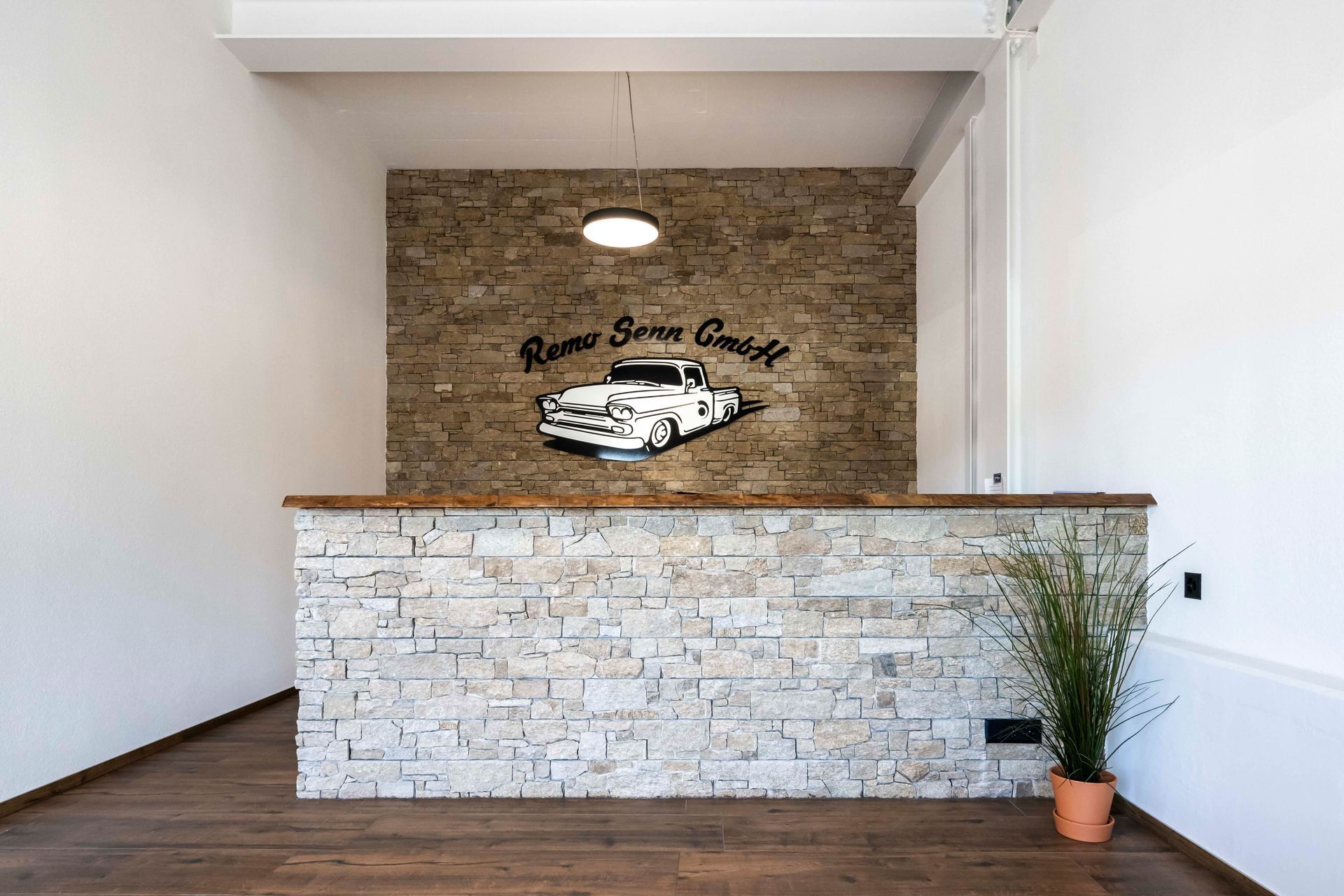 Rezeptionstresen mit Steinfassade, Holztheke, Logo und Autografik an der Wand.