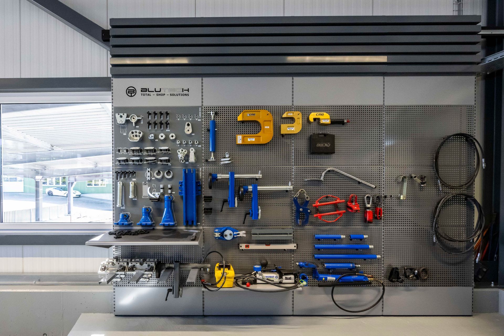 Werkzeuge, die in einer Werkstatt auf einem Wanddisplay angeordnet sind; verschiedene Größen und Farben, darunter Blau, Gelb und Silber.