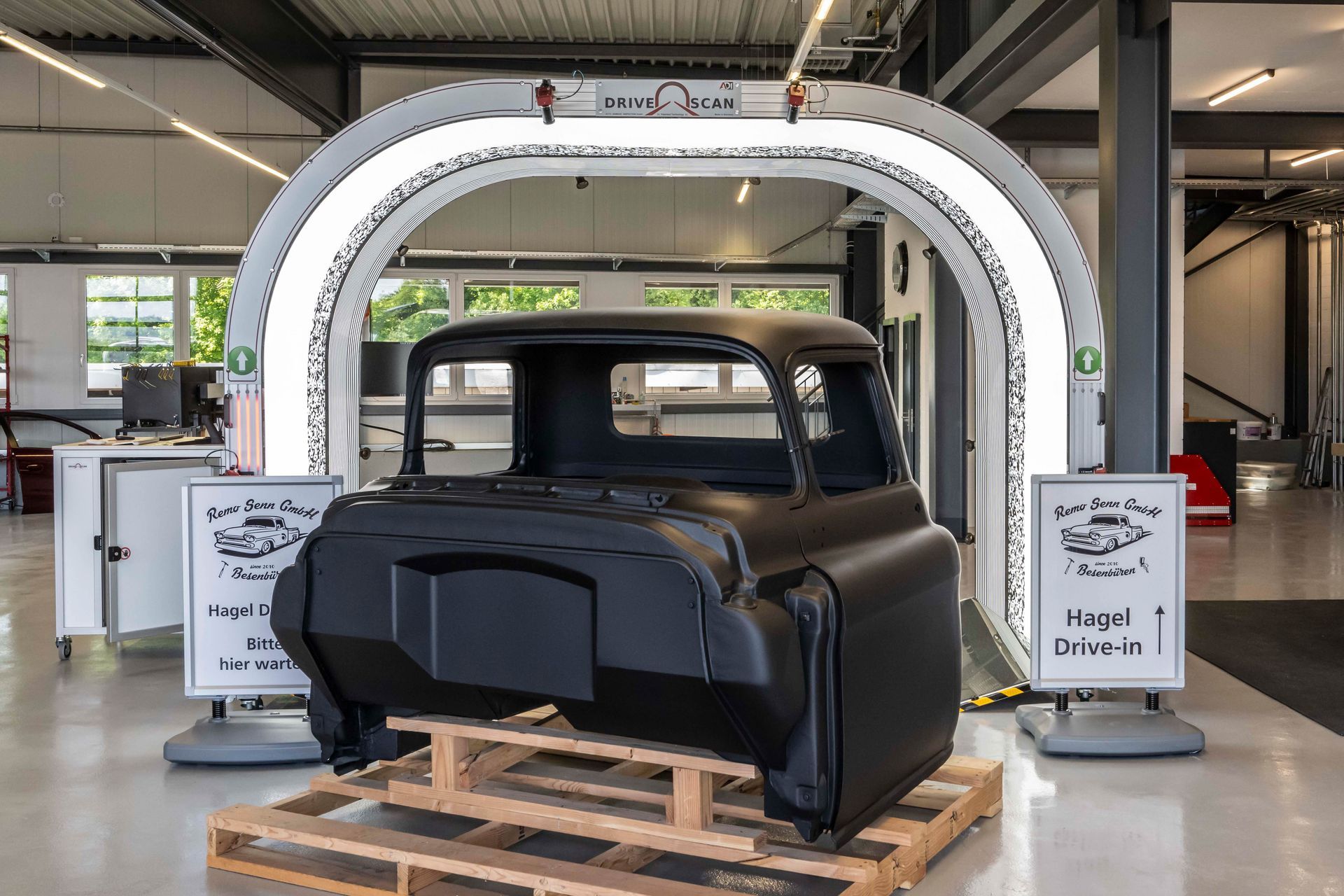 Schwarzes LKW-Fahrerhaus auf einer Palette unter einem großen weißen Ring, wahrscheinlich zur Inspektion in einer Fabrik.