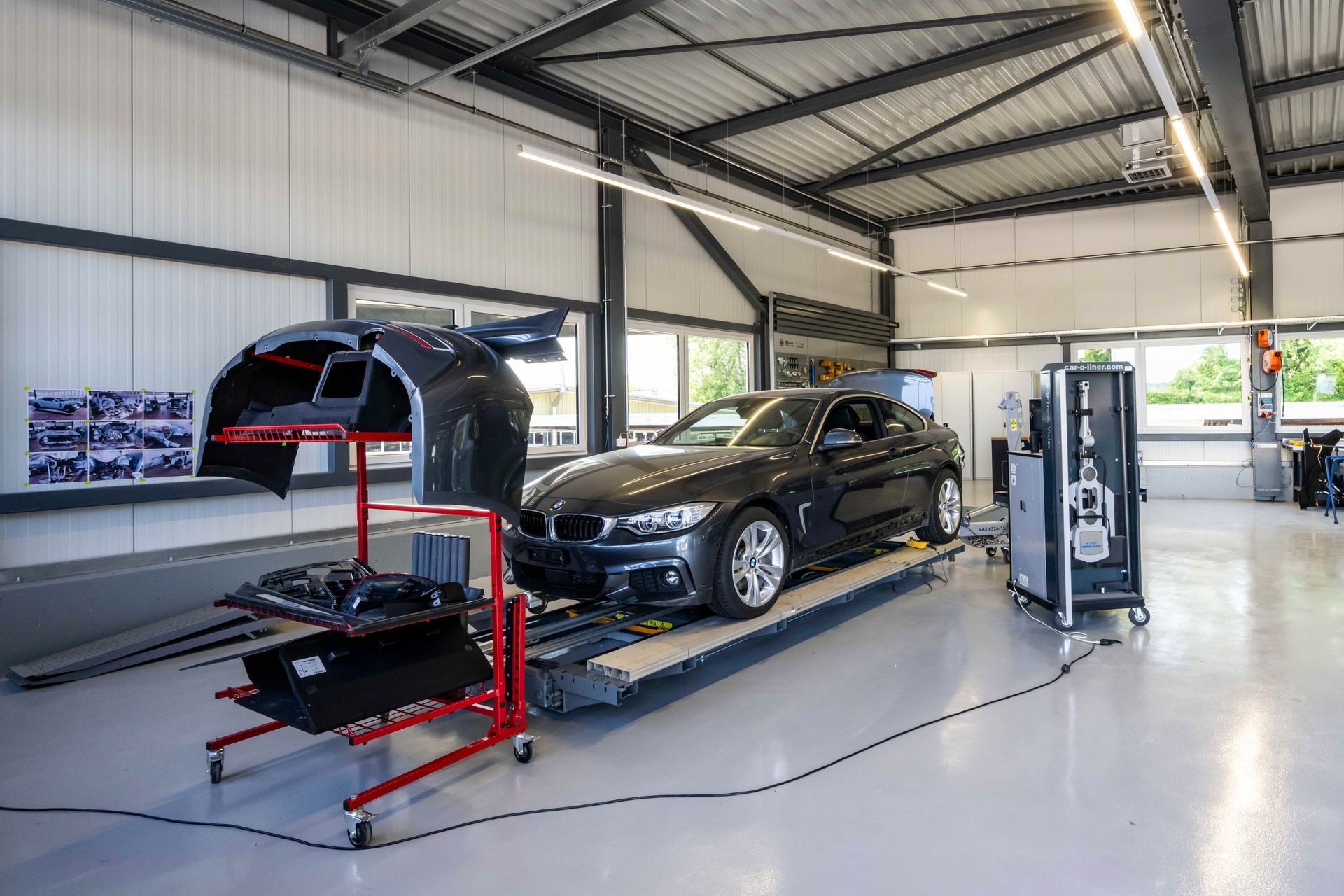 Auto in einer Reparaturwerkstatt auf einer Hebebühne mit Ersatzteilen, ein dunkelgrauer BMW und eine moderne Garagenumgebung.