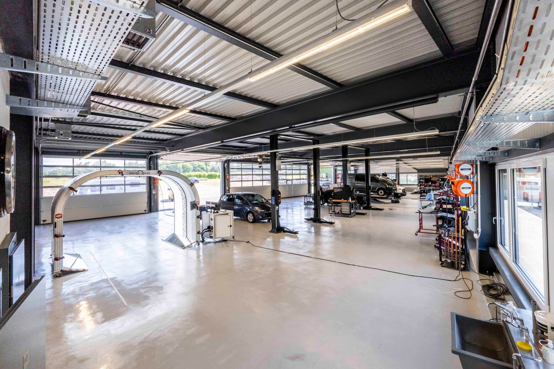 Geräumige Autowerkstatt mit Autos auf Hebebühnen, Werkzeugen und Ausrüstung. Helles, modernes Interieur.