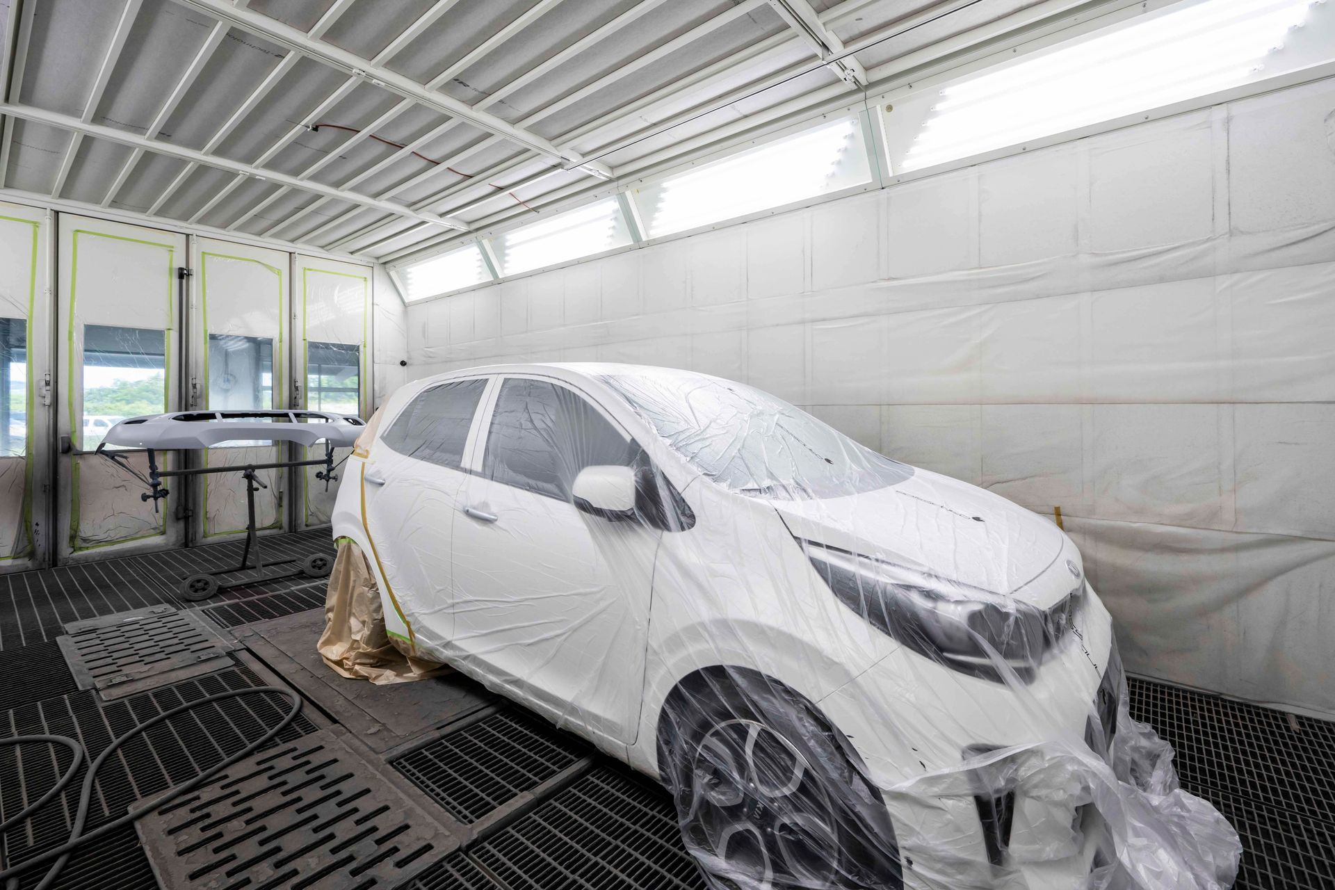 Weißes, mit Plastik bedecktes Auto in einer Lackierkabine, bereit zum Lackieren.