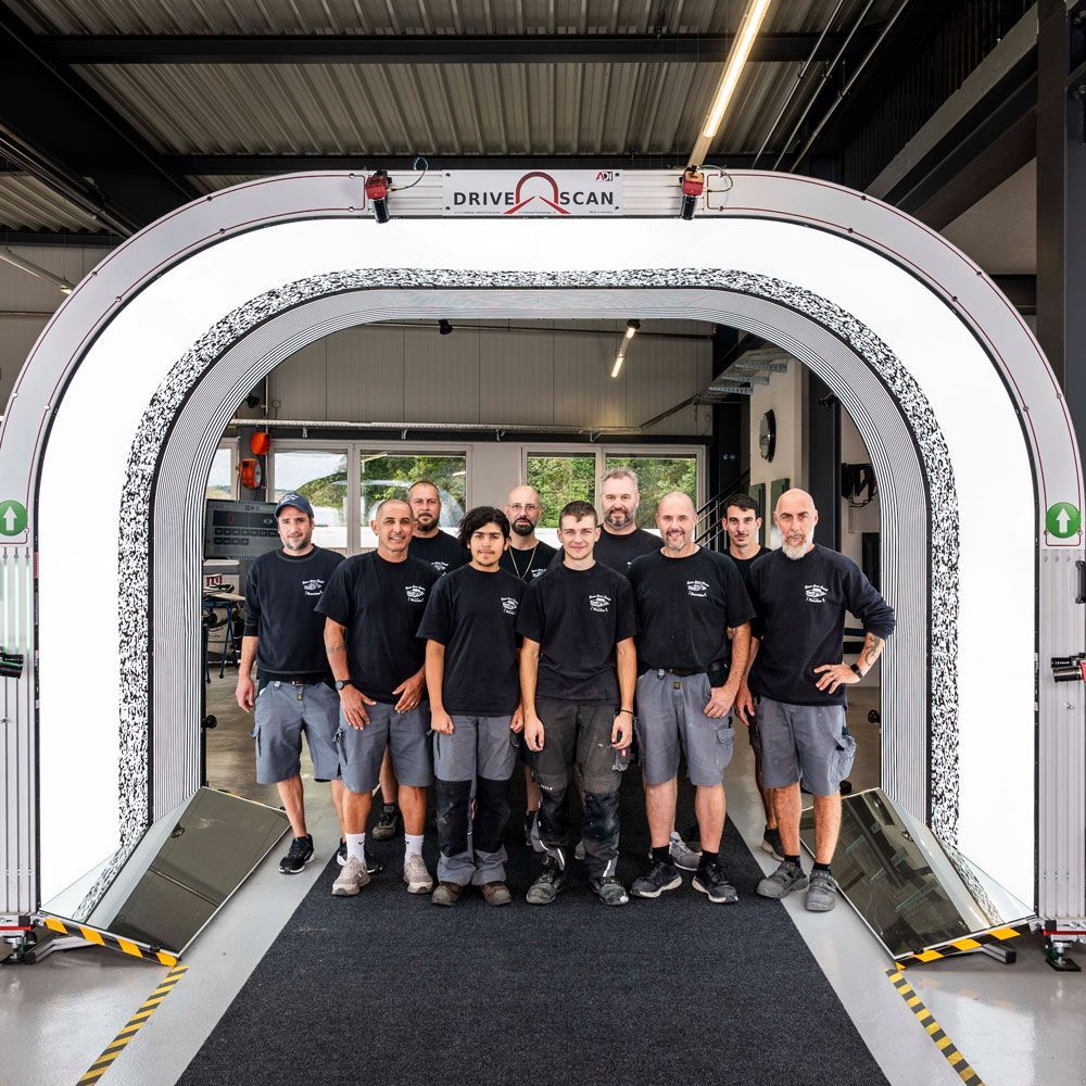 Eine Gruppe von Teammitgliedern steht in einem großen weißen industriellen Scannerbogen; alle tragen einheitliche schwarze Hemden.