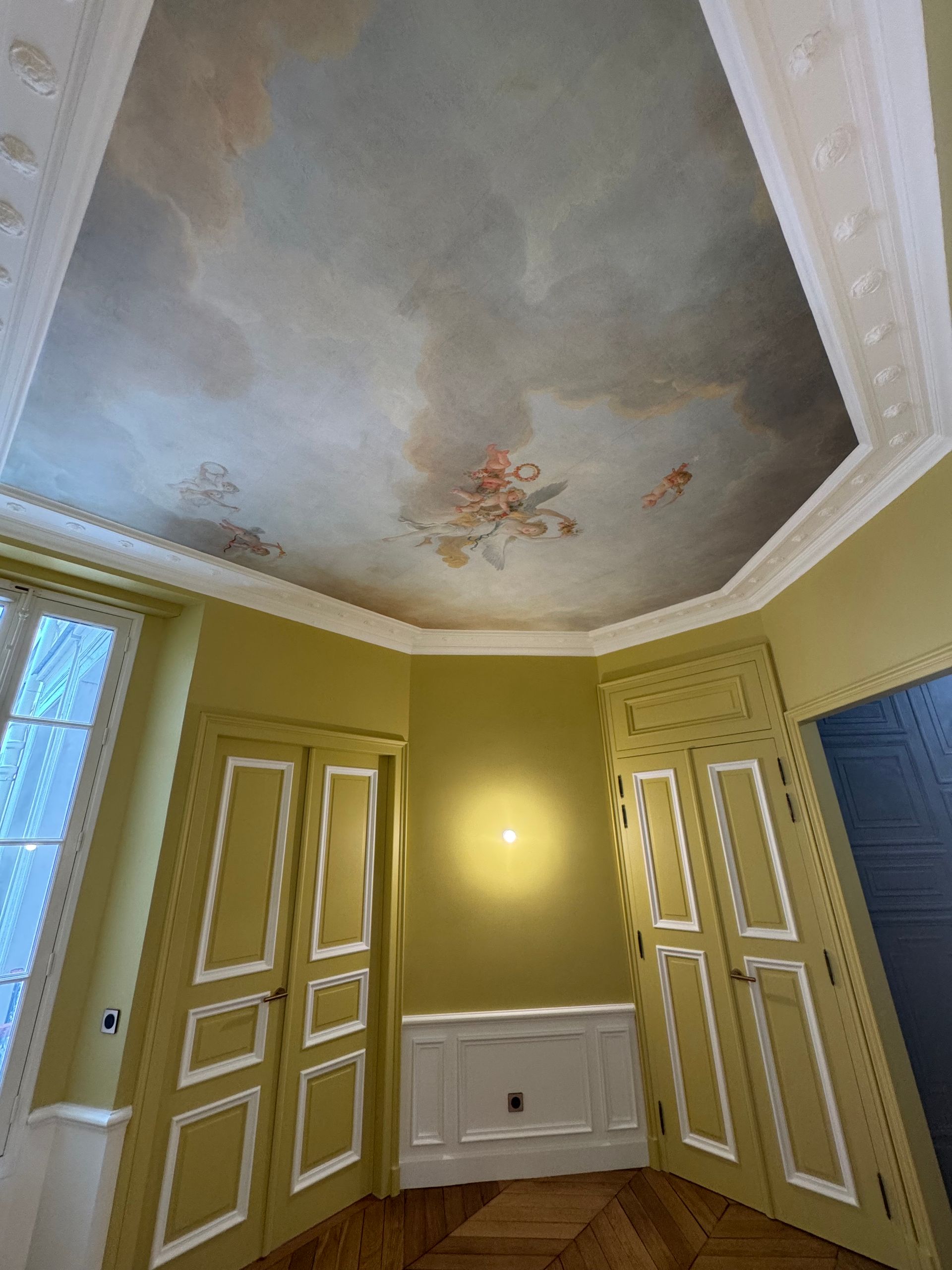 Pièce avec parquet à chevrons, murs jaunes, moulures blanches et plafond peint.