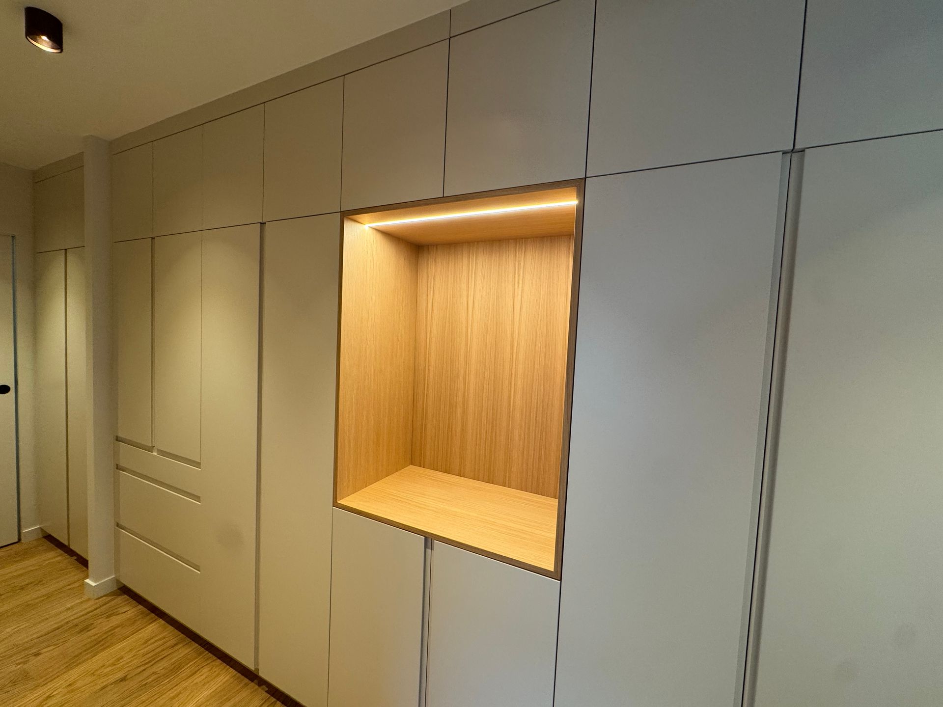 Un homme installe une armoire dans une pièce ; l'armoire possède des étagères blanches et un tiroir en bois.