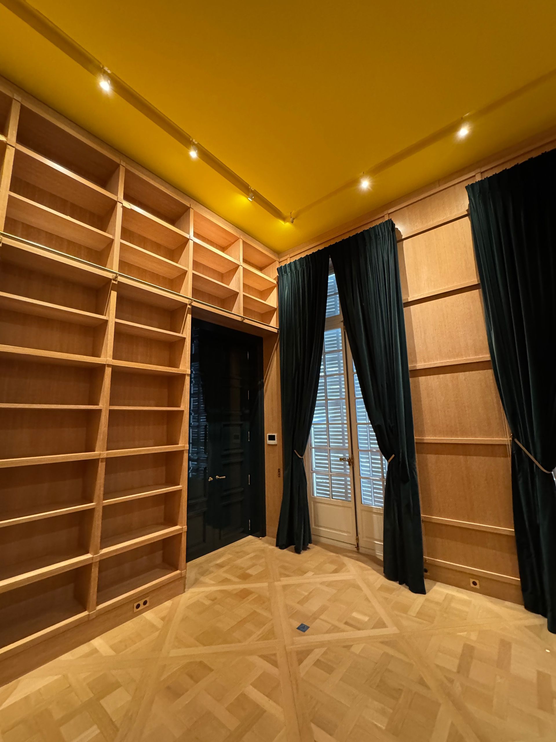 Bibliothèque en bois avec étagères intégrées, rideaux vert foncé et plafond jaune.