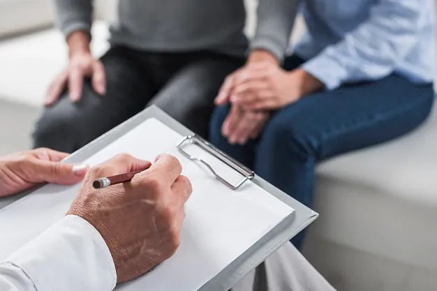 Un hombre está escribiendo en un portapapeles mientras una mujer se sienta a su lado.