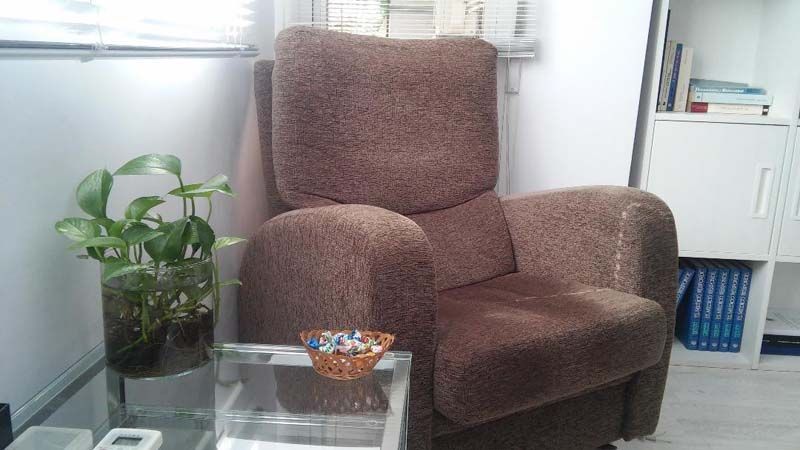 Un sillón reclinable marrón se encuentra junto a una mesa de vidrio en una sala de estar.