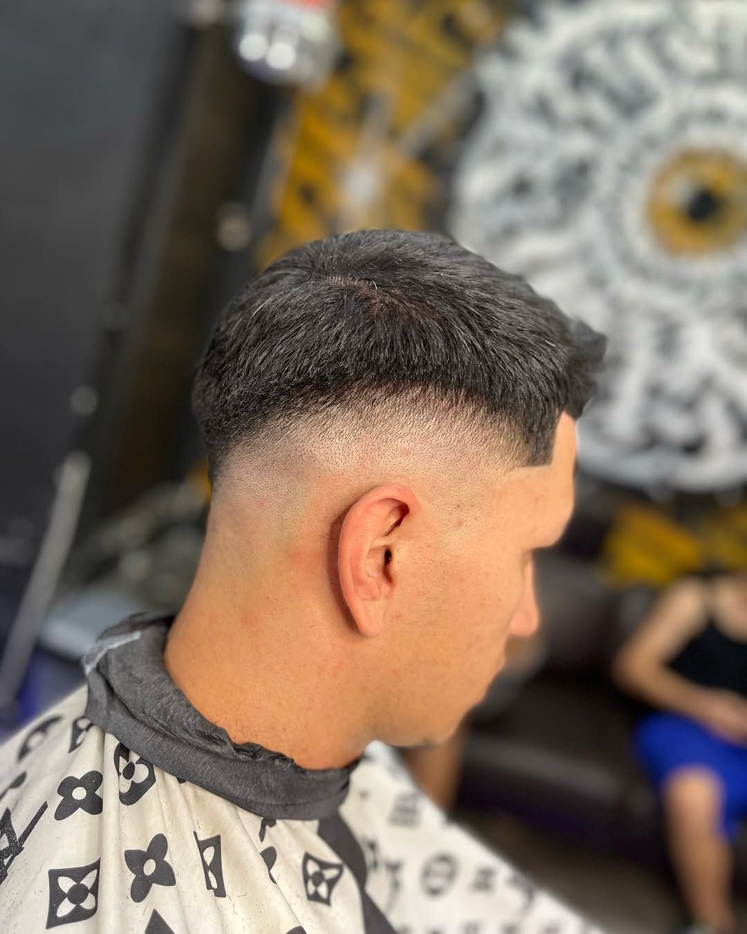 Hombre con un corte de pelo descolorido, vestido con una capa de barbero, sentado en una barbería.