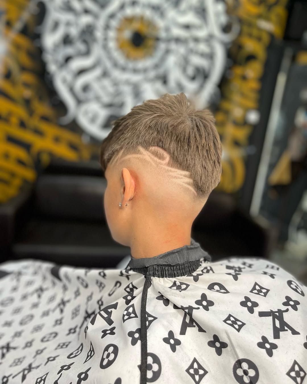 Persona con un corte de pelo que presenta un diseño degradado y afeitado en el costado de la cabeza, vistiendo una capa de barbero.