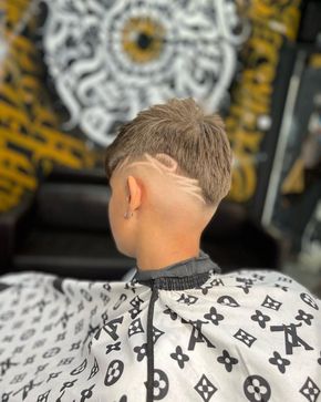 Persona con un corte de pelo que presenta un diseño degradado y afeitado en el costado de la cabeza, vistiendo una capa de barbero.