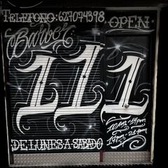 Puerta de barbería en blanco y negro con letras estilizadas y horario. Se ve la palabra "Barber".