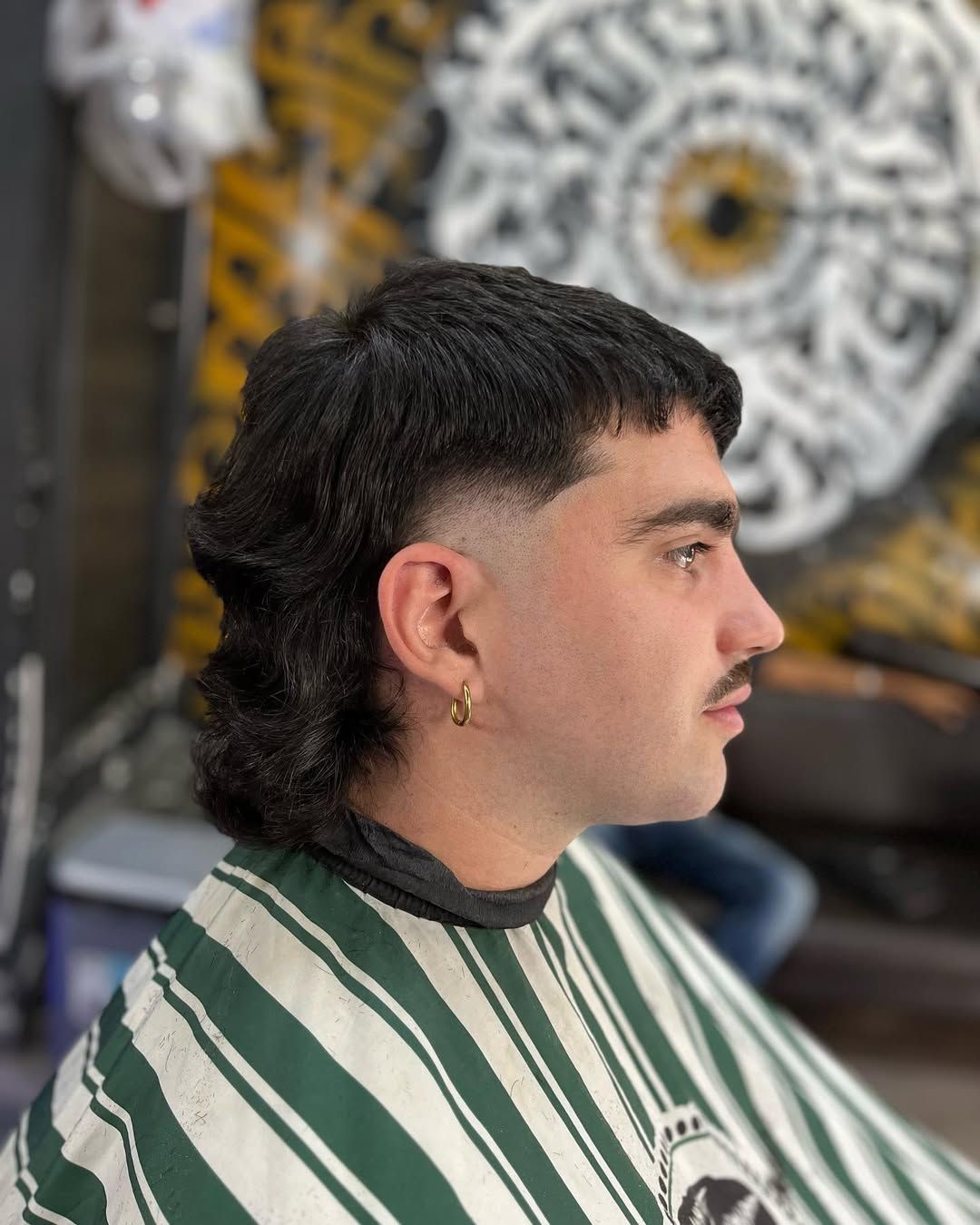 Hombre con corte de pelo mullet, degradado a los lados, vistiendo una capa en una barbería.