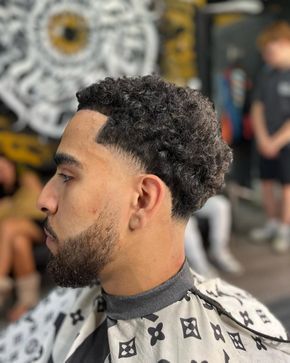 Hombre con cabello rizado, corte descolorido y barba recortada, en una barbería.