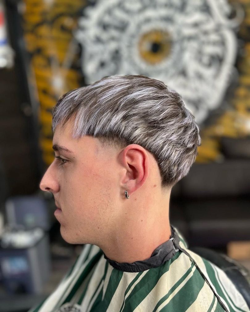 Hombre con corte de pelo degradado y flequillo, mirando a la izquierda. Lleva una capa de barbero en una peluquería.
