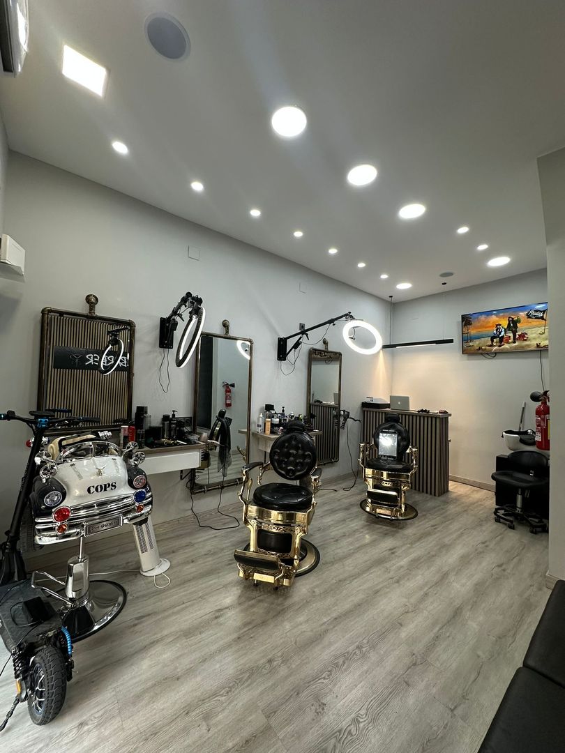 Interior de barbería con sillas, espejos, iluminación y herramientas. Sillas doradas y negras.