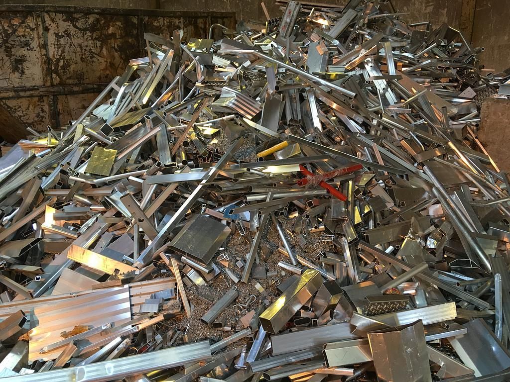 Tas de ferraille, comprenant des poutres et des tôles, dans un environnement industriel sombre.