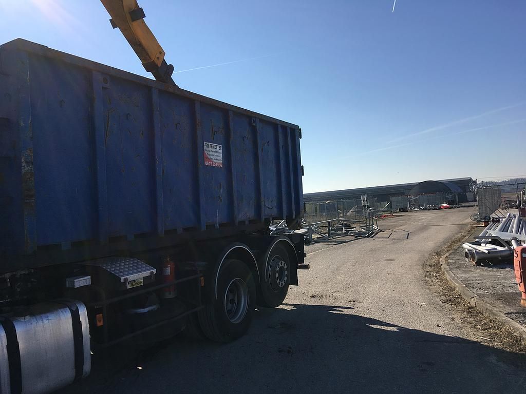 Un camion bleu transportant un conteneur se trouve dans une casse par une journée ensoleillée.