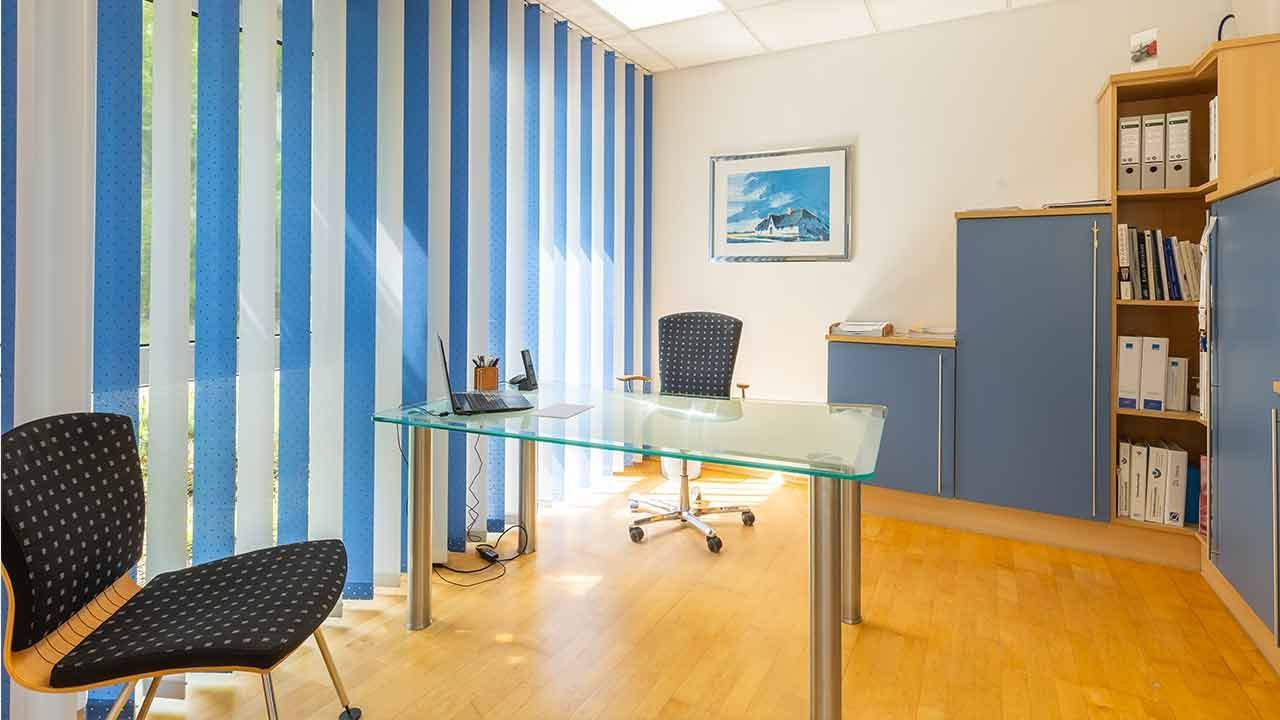 Ein Zimmer mit Schreibtisch und Stühlen und blauen und weißen Jalousien