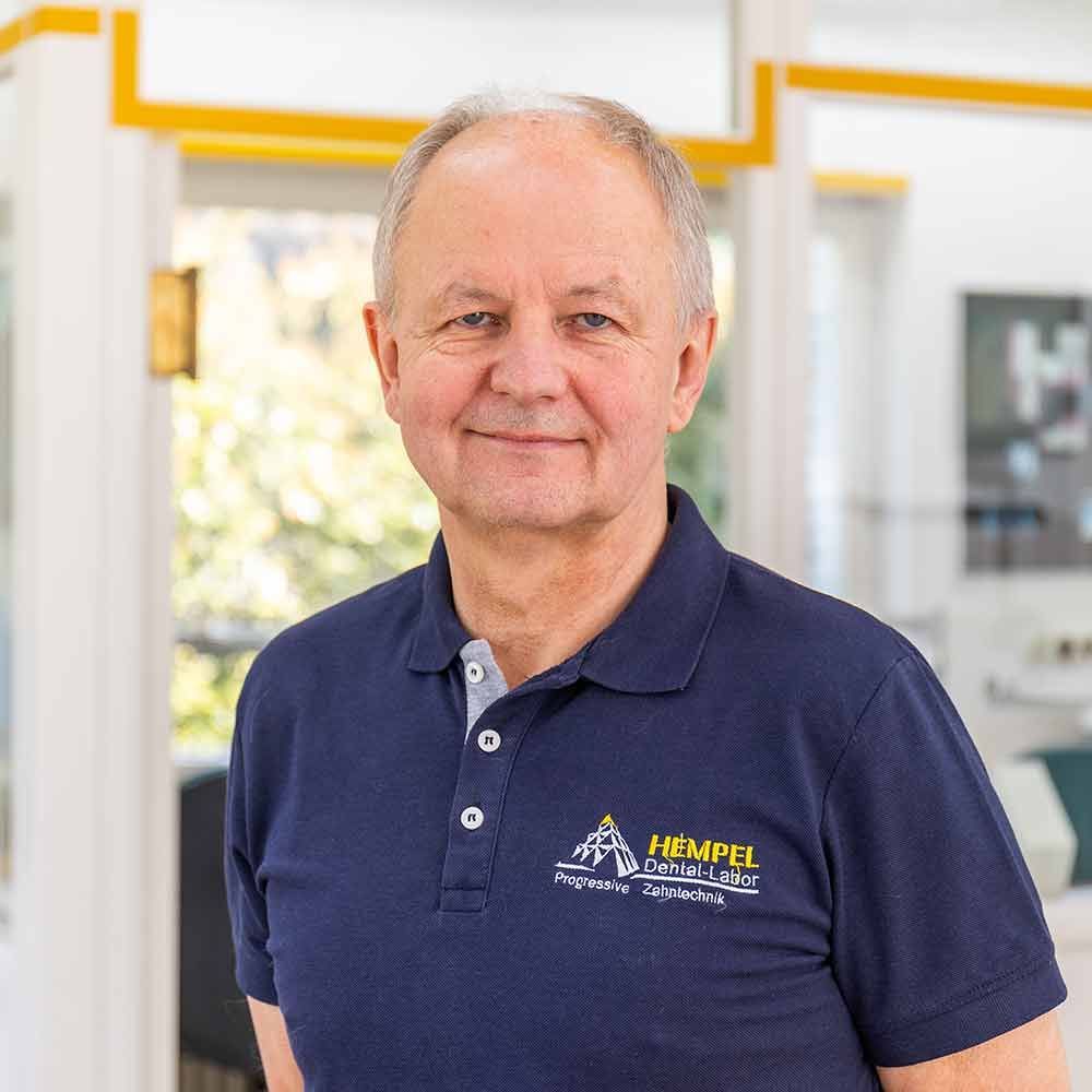 Ein Mann in einem blauen Poloshirt lächelt in die Kamera.