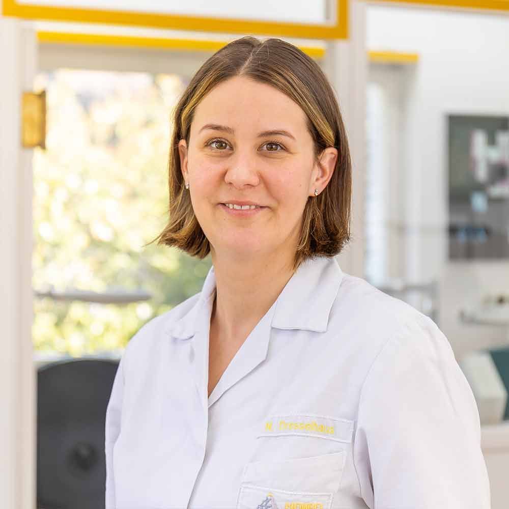 Eine Frau im weißen Laborkittel lächelt in die Kamera.