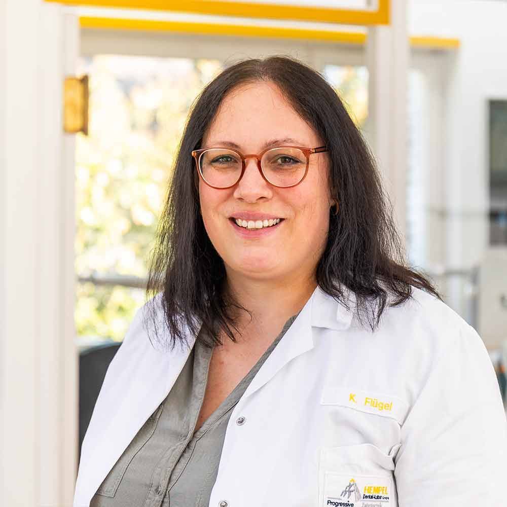 Eine Frau mit Brille und weißem Laborkittel lächelt in die Kamera.