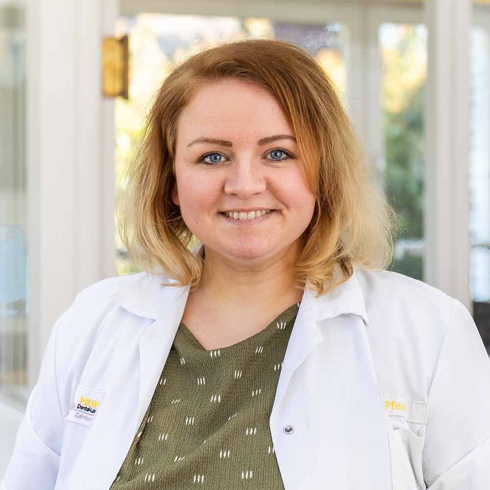 Eine Frau im weißen Laborkittel lächelt in die Kamera.