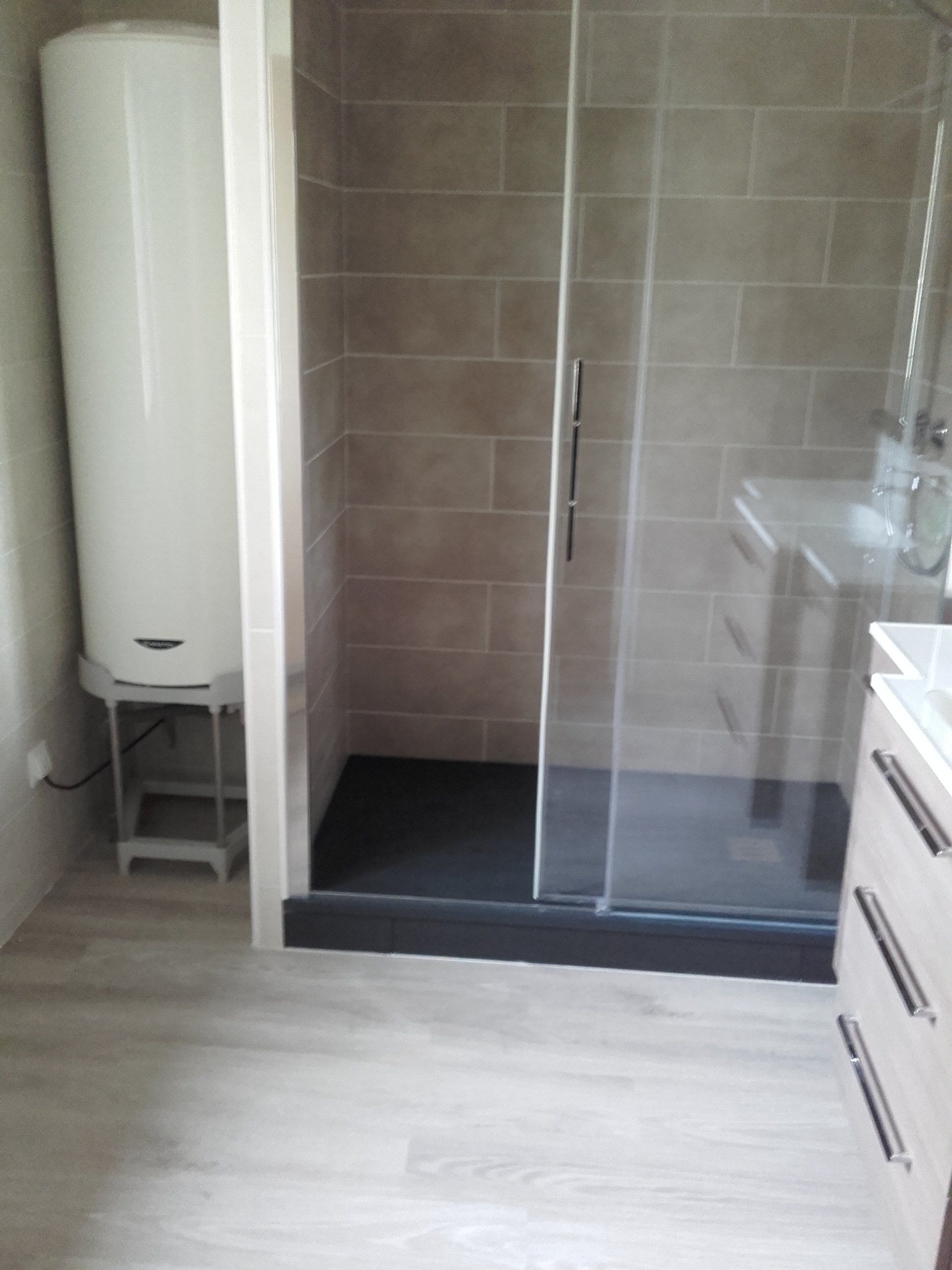 Salle de bain avec douche, chauffe-eau, vanité et plancher de couleur claire.