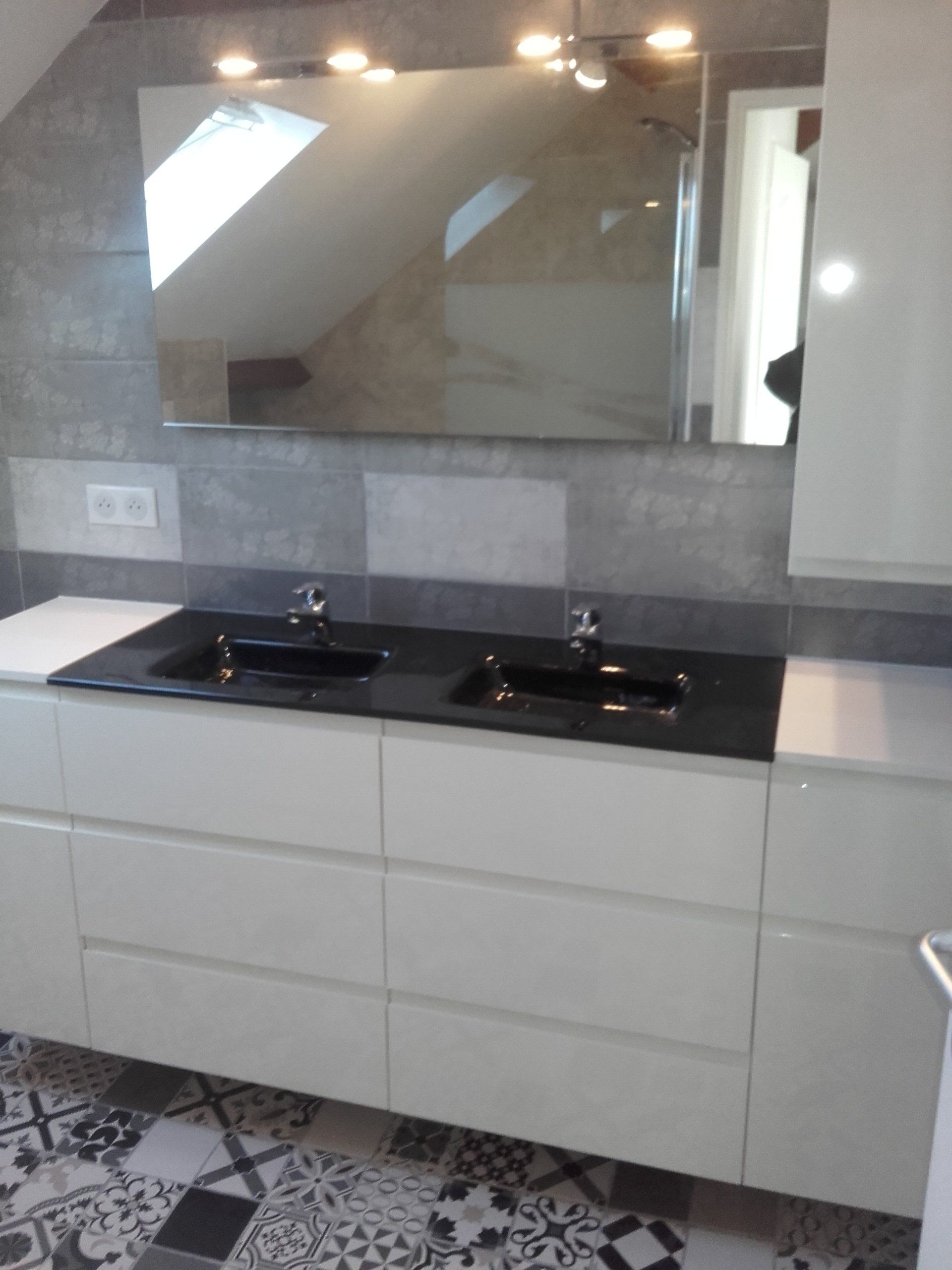 Salle de bain moderne avec vanité blanche, lavabos noirs, grand miroir et sol en carrelage à motifs.