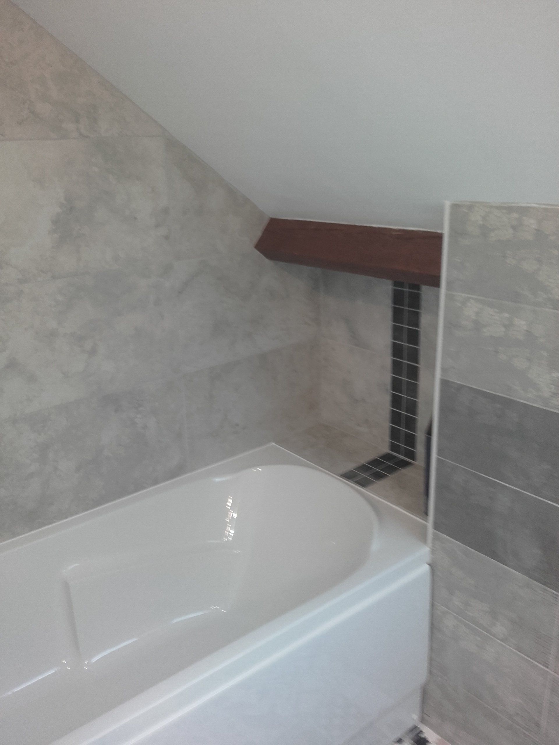 Baignoire dans la salle de bain avec mur en angle, poutre brune et murs carrelés.