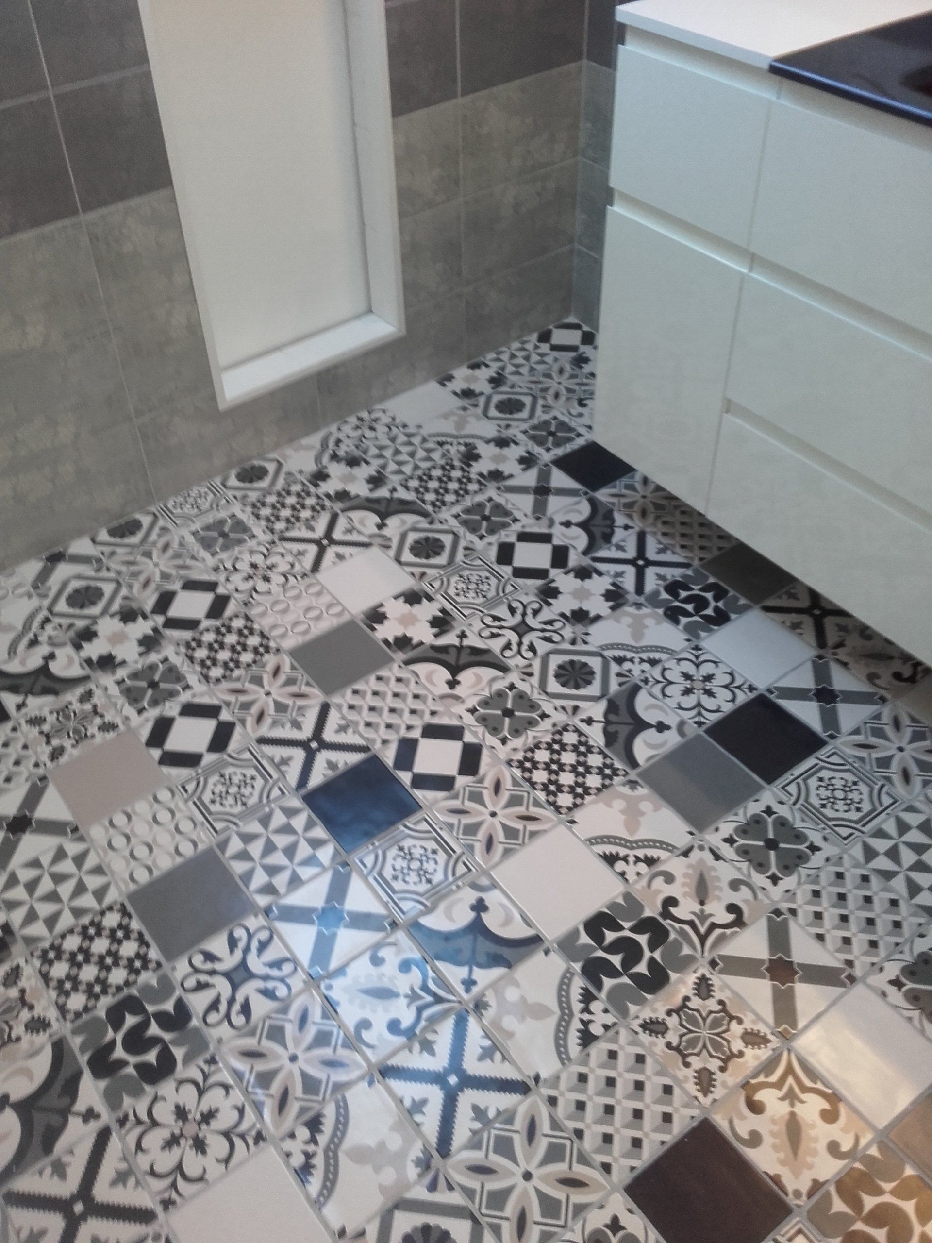Sol de cuisine avec carrelage à motifs en noir, blanc et gris, à côté d'armoires blanches.