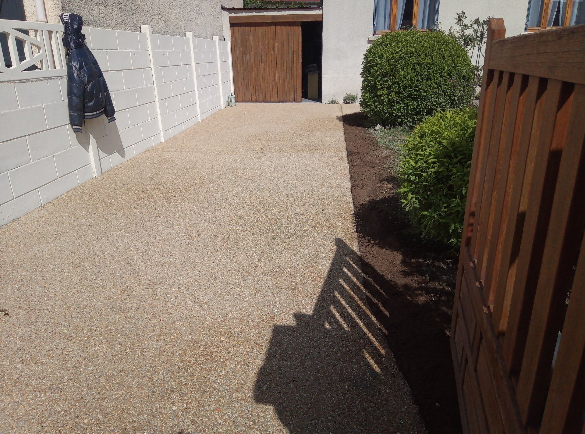 Allée de gravier bordée d'une clôture blanche et d'un portail en bois ; un manteau est accroché à la clôture.