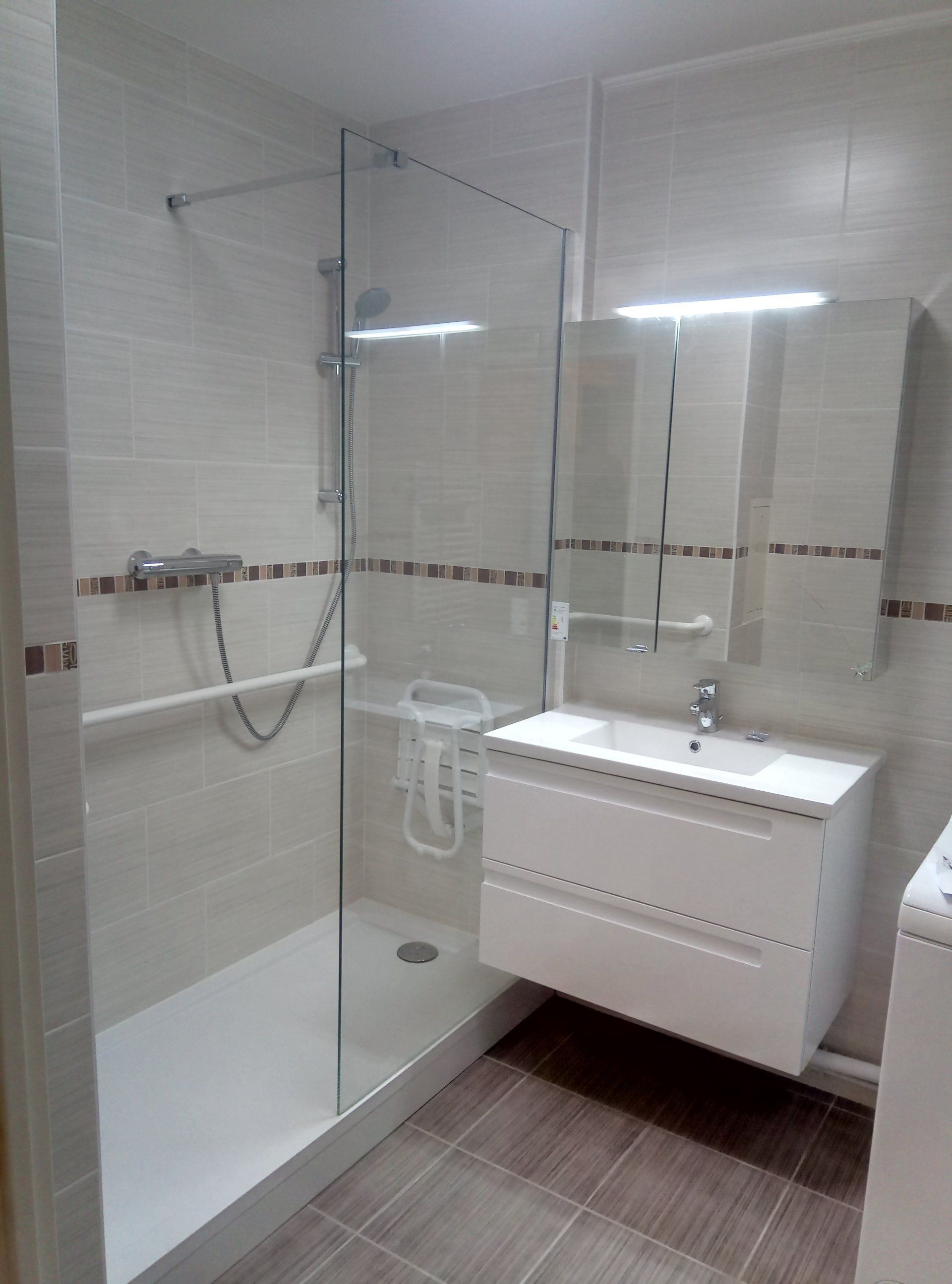 Salle de bain accessible avec douche en verre, vanité blanche, barre d'appui et option de douche assise.