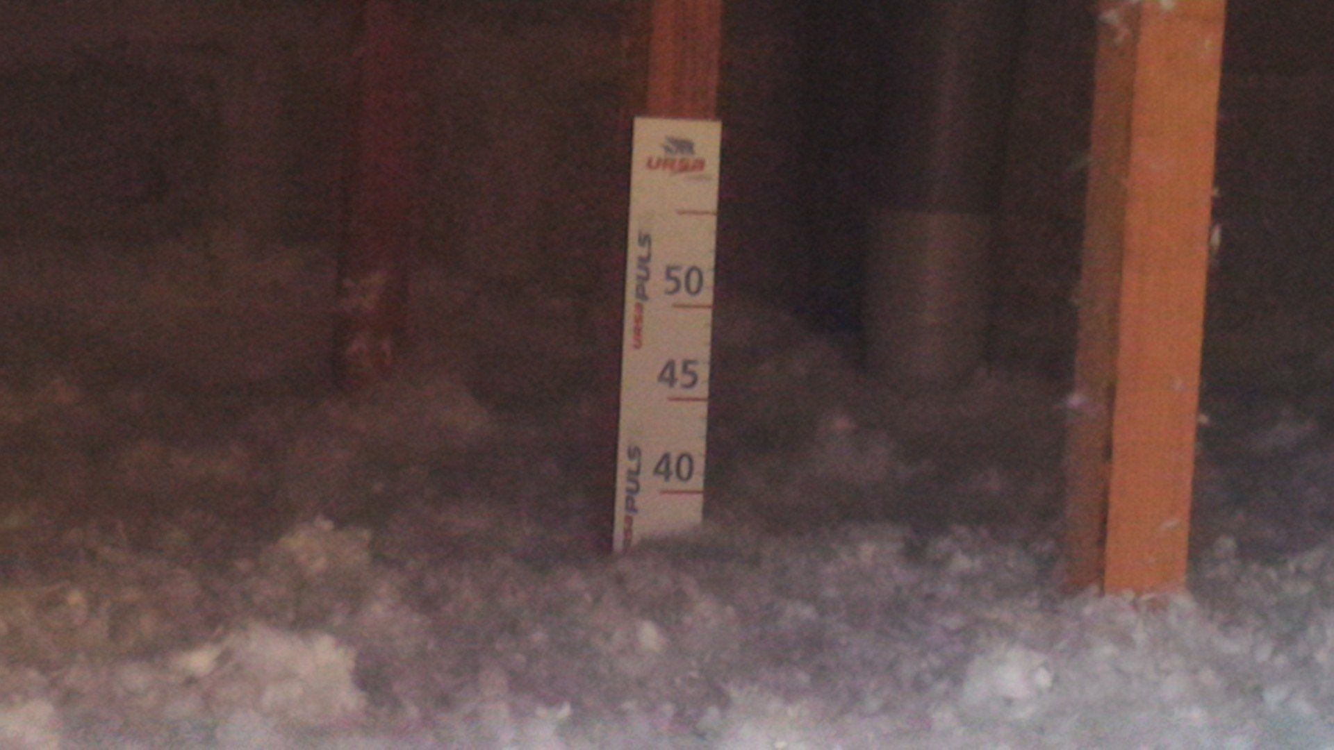 Grenier avec isolation, un guide de mesure indiquant 40, 45 et 50 pouces et des poutres en bois.