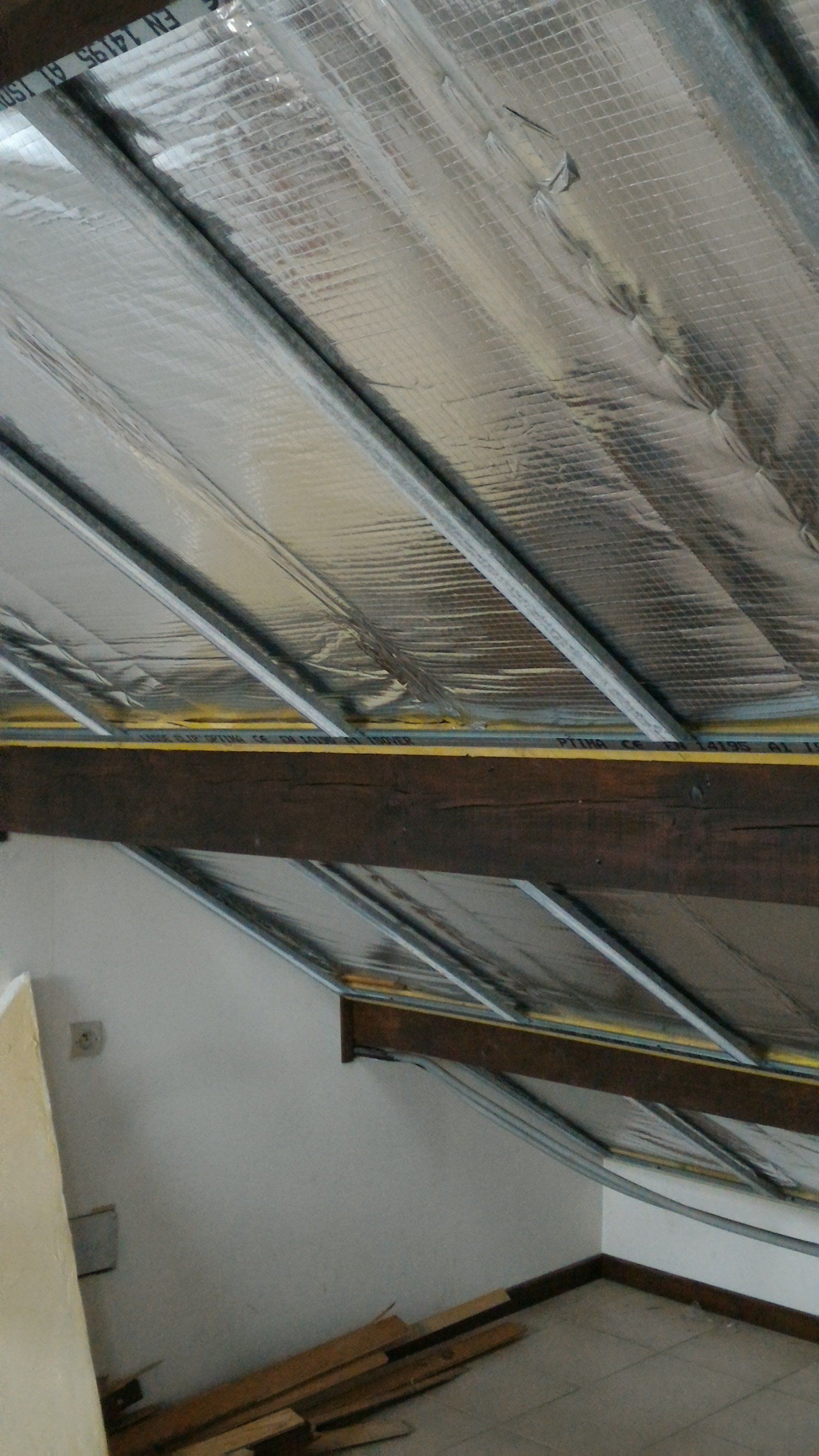 Plafond avec isolation argentée entre poutres métalliques, poutres en bois en dessous.