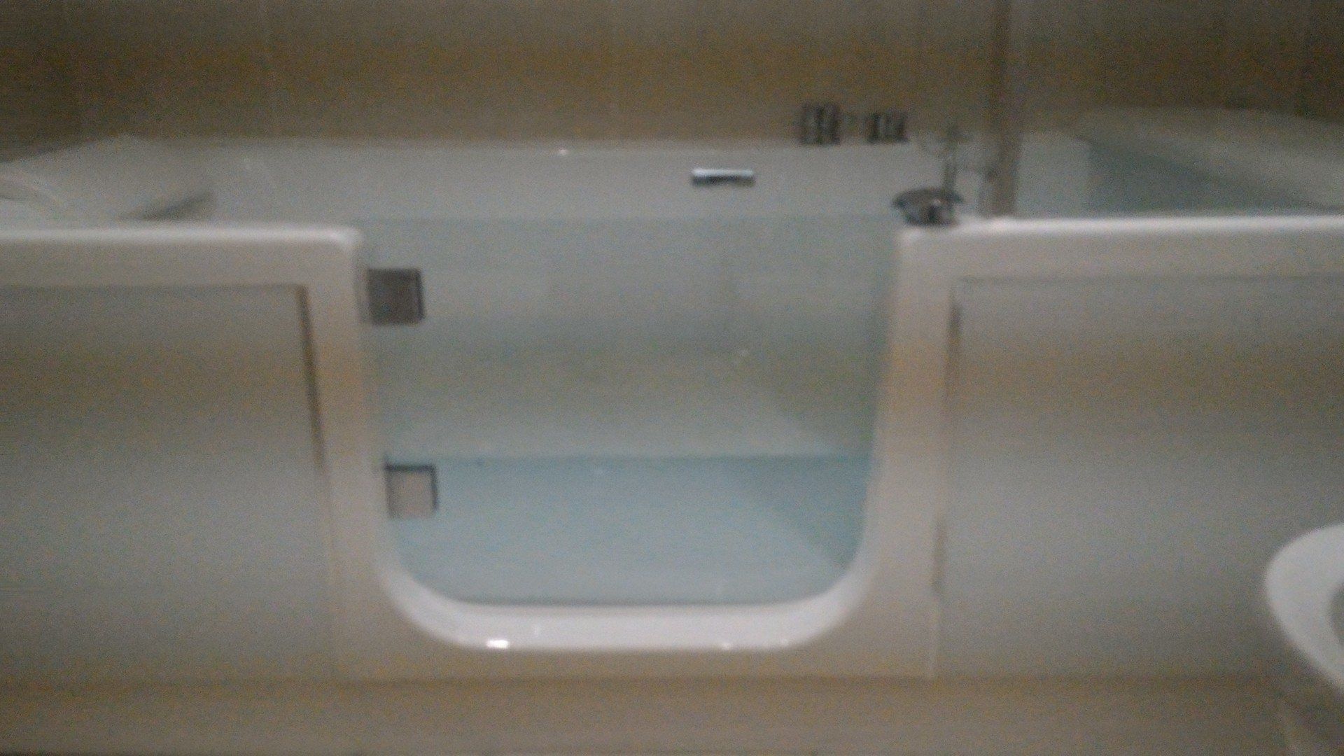 Baignoire blanche à l'italienne avec une porte transparente et ouverte remplie d'eau dans une salle de bain.