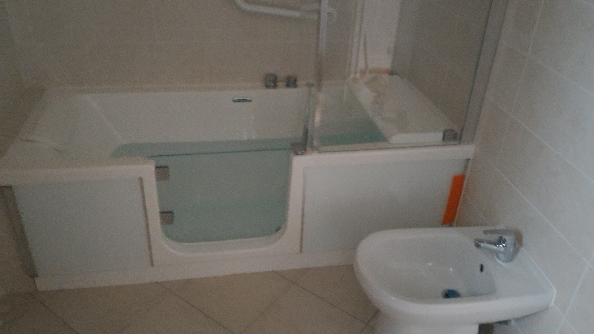 Baignoire blanche à l'italienne avec porte et bidet dans une salle de bain.