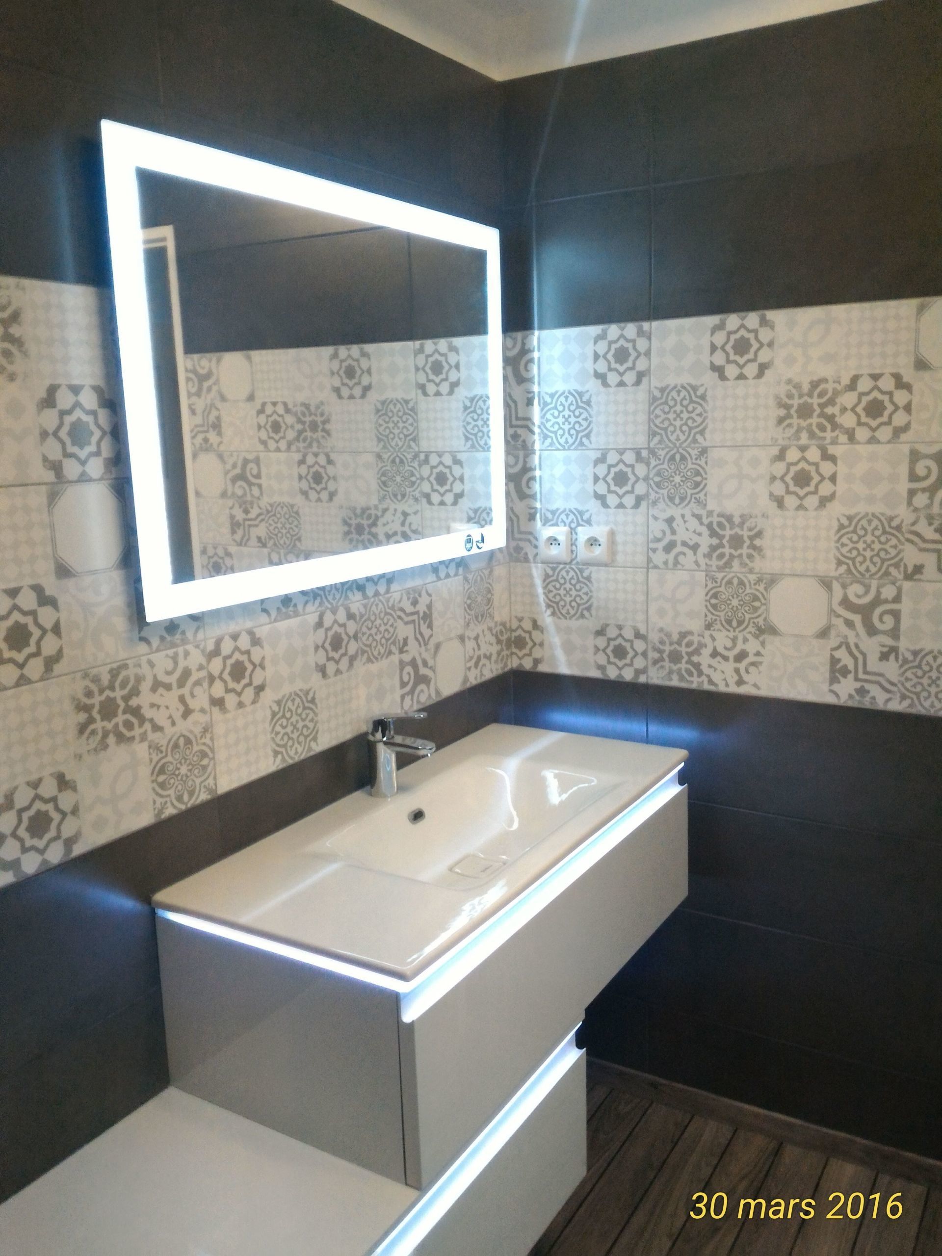 Salle de bain moderne avec miroir éclairé et meuble-lavabo. Crédence en carrelage à motifs.