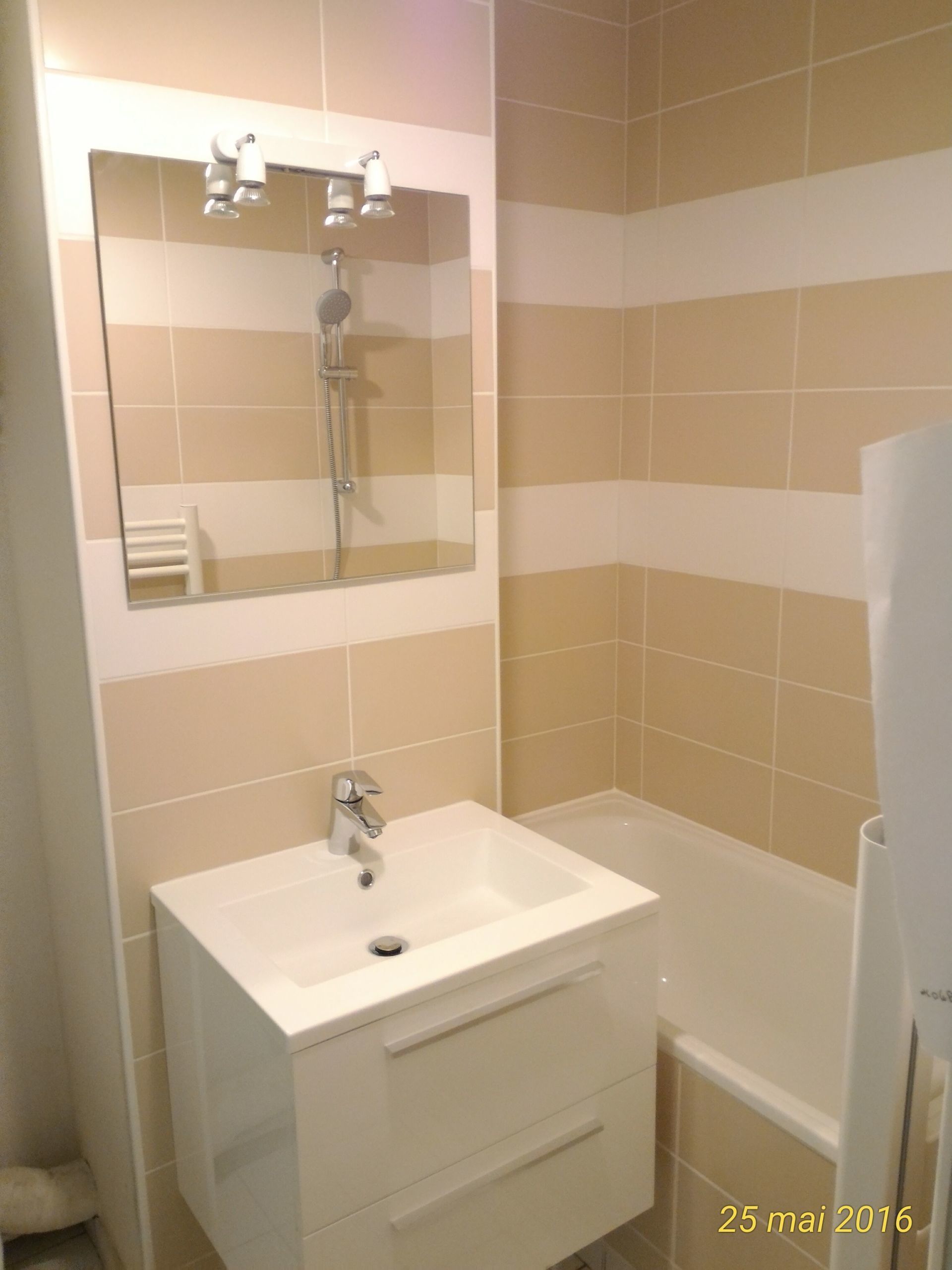 Salle de bain avec meuble-lavabo blanc, miroir et baignoire. Murs carrelés à rayures crème et blanches.