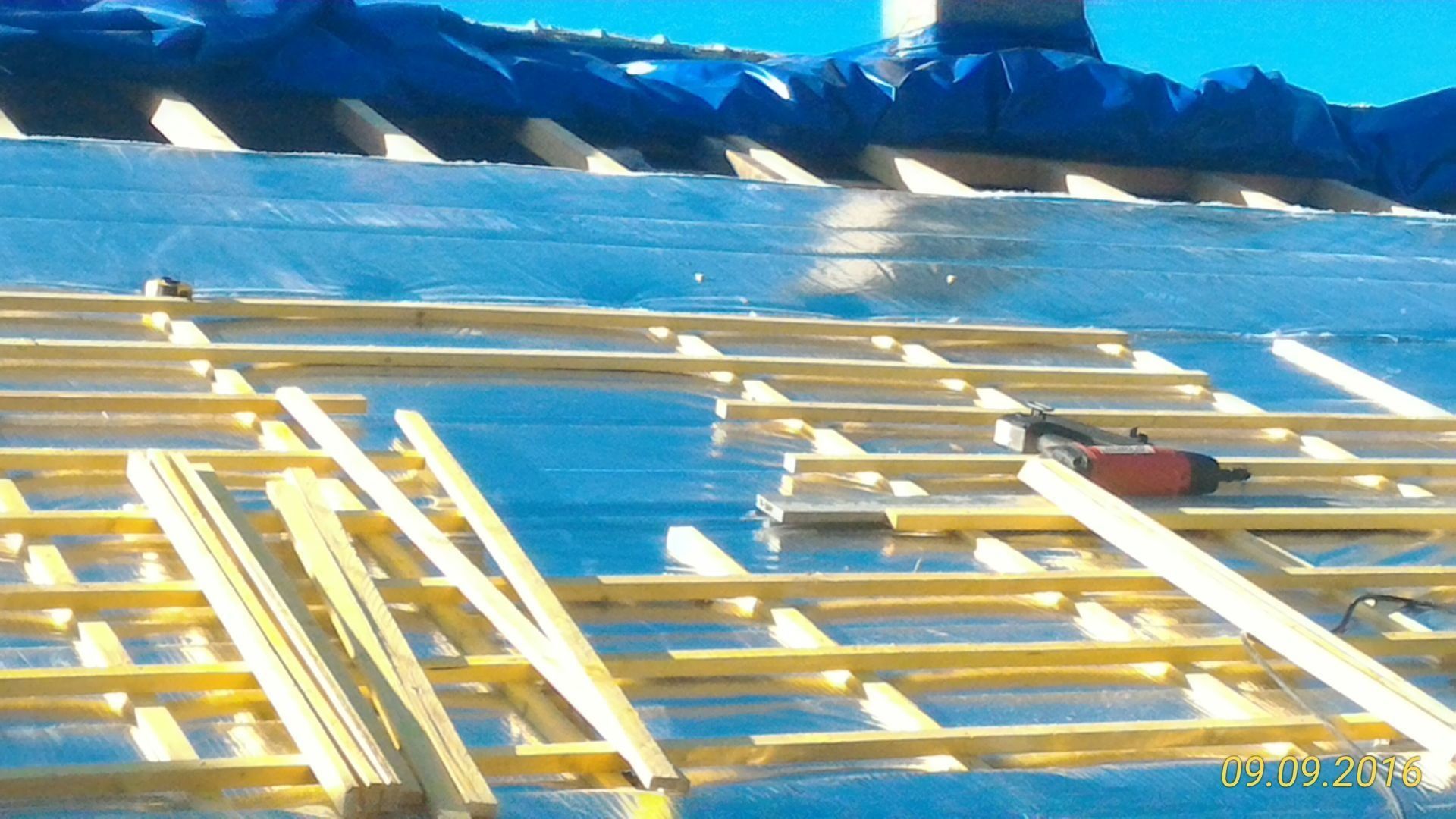 Construction de toiture avec poutres en bois, sous-couche métallique et bâche bleue.